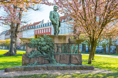 A bronze statue of Viggo Horup stands proudly in the tranquil Rosenborg Castle Garden, surrounded by blooming cherry trees and historic buildings in Copenhagen, Denmark.の写真素材