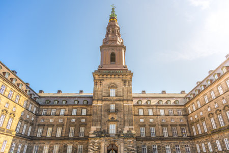 Visitors admire the stunning architecture of Christiansborg Palace in Copenhagen, surrounded by historical charm under a bright blue sky. The grandeur of this government building captivates all.の写真素材