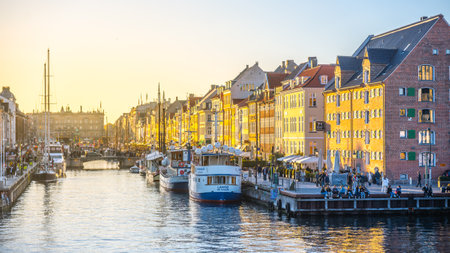 Nyhavn in Copenhagen showcases a stunning sunset, casting a warm glow on the colorful buildings and bustling waterfront. People enjoy the lively atmosphere along the canal.の写真素材
