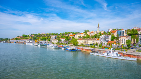 The Sava River flows through Belgrade, showcasing vibrant buildings and lush greenery along the banks. Boats are docked, and the skyline reveals a mix of history and modernity.の写真素材
