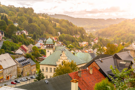 A breathtaking view of Jachymov reveals charming architecture surrounded by lush hills. The sunset bathes the town in warm tones, showcasing its historic buildings and serene atmosphere.の写真素材