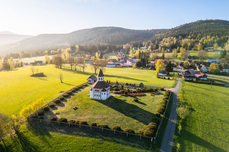 Tesarov Chapel, a striking white octagonal structure, stands amidst lush greenery in Korenov, surrounded by the picturesque Jizera Mountains. The serene landscape basks in soft sunlight.の写真素材