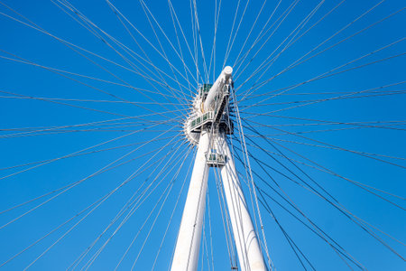 This detailed view showcases the intricate design of the London Eyes wheel and cables, highlighting its architectural beauty against a vibrant blue sky in London.の写真素材