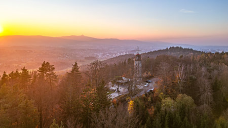 The lookout tower stands majestically on Prosec Ridge, overlooking Jablonec nad Nisou as the sun sets behind the Jizera Mountains, casting warm colors over the landscape.の写真素材