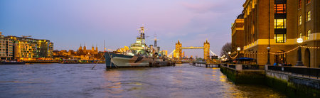 HMS Belfast rests on the Thames River during evening hours, with Londons iconic landmarks...