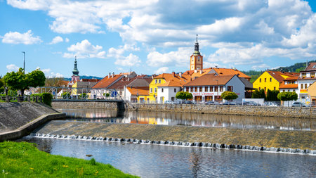 The Otava River flows gently through Susice, showcasing quaint buildings with vibrant colors. Fluffy...