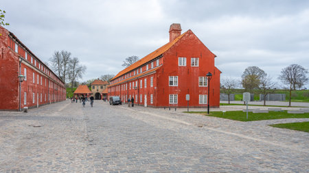 Kastellet barracks in Copenhagen features striking red buildings set against a cloudy sky. Visitors stroll through this historical site, enjoying the charm of the well-preserved structures.の写真素材