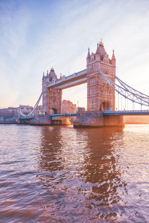 Tower Bridge stands majestically as the sun rises, casting warm hues over the Thames River. This iconic landmark is illuminated, showcasing its architectural beauty at dawn.の写真素材