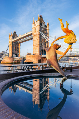 Girl with a Dolphin - a vibrant statue features a girl joyfully interacting with a dolphin, set against the iconic Tower Bridge in London. The sun illuminates the scene, creating a picturesque moment.の写真素材