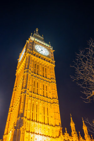 Big Ben stands majestically against the night sky, its clock face glowing warmly. The surrounding architecture showcases intricate designs, reflecting the historic charm of London.の写真素材