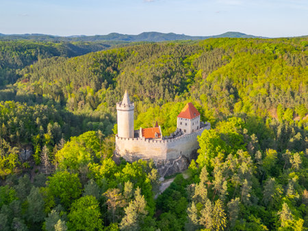 Kokorin Castle stands majestically amidst lush greenery in Czechia during a sunny evening. The aerial view showcases its ancient architecture surrounded by rolling hills and vibrant trees.の写真素材