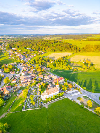 Bohutin Town showcases a picturesque landscape with lush fields and quaint homes. The historic church and cemetery are prominent features, illuminated by the warm glow of sunset.の写真素材