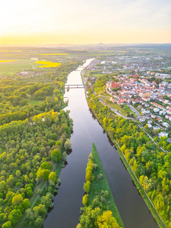 Stunning aerial perspective of the confluence of Vltava and Labe rivers by Melnik in Czechia. Lush green banks meet flowing waters under a golden sunset sky.の写真素材