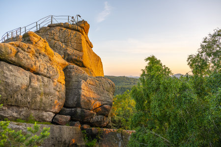 The warm glow of sunset illuminates the sandstone Popov Cliffs in Czechia. Lush greenery surrounds the rocky formation, showcasing the beauty of nature in the evening light.の写真素材