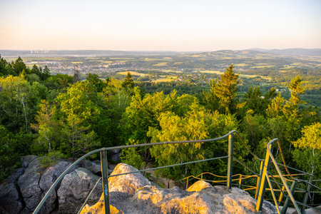 Enjoy breathtaking views from Popov Cliffs in the Lusatian Mountains as the sun sets, casting golden hues over lush landscapes and the charming valley below.の写真素材