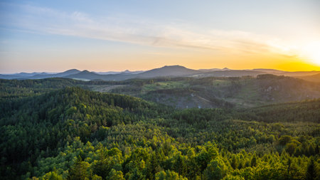 A breathtaking sunset casts golden hues over the Lusatian Mountains, viewed from the heights of Popov Cliffs. Dense forests stretch across the landscape, creating a serene evening atmosphere.の写真素材