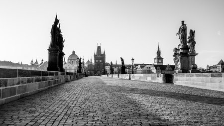 Sunrise casts a golden hue over Charles Bridge in Prague, revealing the cobblestone path and statues lining the bridge. The calm Vltava River reflects the city historic architecture.の写真素材