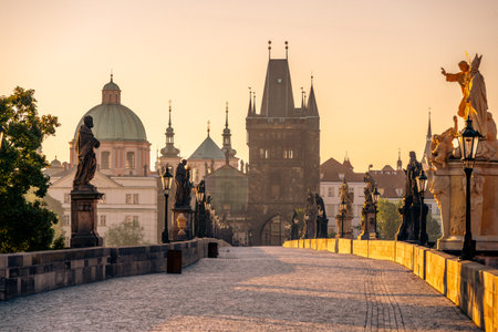 Sunrise casts a warm glow over Charles Bridge in Prague, highlighting the statues and the historic architecture. The Vltava River glistens, creating a serene morning atmosphere.の写真素材
