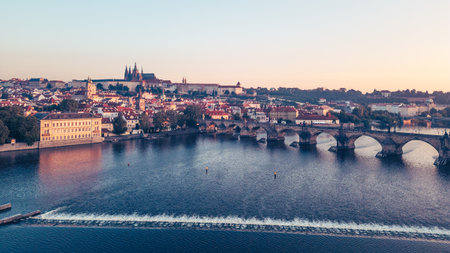 Golden light bathes the medieval architecture of Prague at sunrise, showcasing the Vltava River and the iconic Charles Bridge. Hradcany Castle stands majestically on the hill in the background.の写真素材