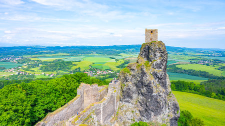 Nestled in the scenic Bohemian Paradise, Trosky Castle Ruins stand atop a rocky outcrop, offering stunning views of the lush green landscape and distant villages under a clear sky.の写真素材