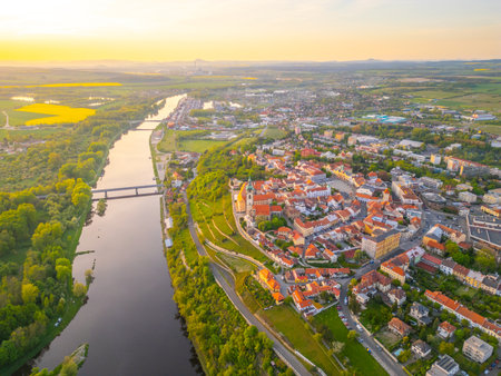 This breathtaking aerial view captures Melnik City and its historic Chateau overlooking the serene Labe River in Czechia. The landscape showcases lush greenery and charming architecture during sunset.の写真素材