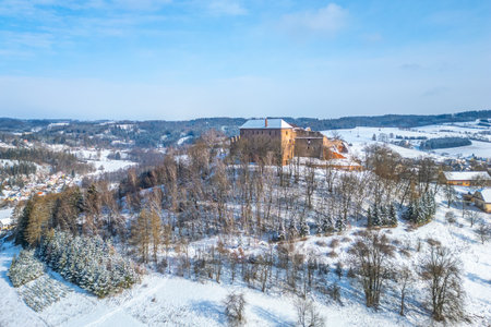 Pecka castle stands majestically atop a hillside covered in fresh snow. The tranquil winter landscape features a clear blue sky and distant hills, enhancing the castles historic charm.の写真素材