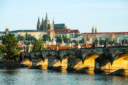 Early morning light illuminates Charles Bridge with Prague Castle in the background. The peaceful Vltava River reflects the stunning architecture, showcasing a tranquil urban landscape.の写真素材