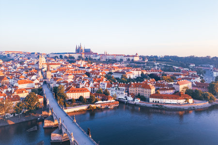Morning light casts a warm glow over Prague, illuminating the cityscape and medieval architecture of Hradcany and the iconic Charles Bridge. A peaceful view of the city at dawn.の写真素材