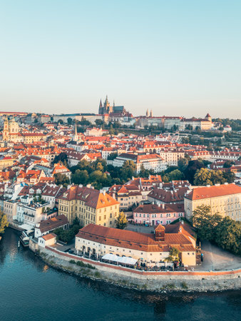 A stunning aerial view of Prague Castle towering above the picturesque Lesser Town, with the Vltava River gracefully flowing through the vibrant cityscape during golden hour.の写真素材