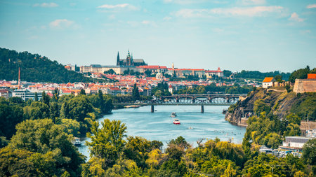 This panoramic view showcases the beauty of Prague, featuring the iconic Prague Castle and the Vltava River. Lush greenery and boats add to the charm of this historical cityscape.の写真素材