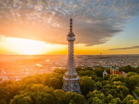 At sunrise, the Petrin Lookout Tower in Prague rises above a lush park, bathed in golden light, offering breathtaking views of the city and the surrounding landscape.の写真素材