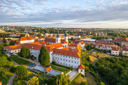 Strahov Monastery reveals its stunning architecture illuminated by the soft morning light. An aerial view showcases the vibrant red roofs and lush surroundings at dawn in Prague.の写真素材