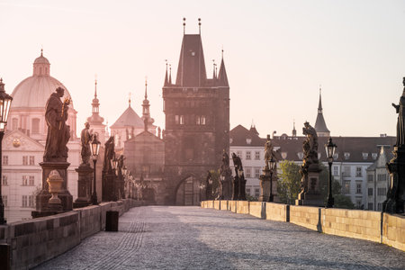 Early morning light bathes Charles Bridge in a golden hue, illuminating its historic statues and towers. The quiet Vltava river reflects the serene beauty of the scene.の写真素材