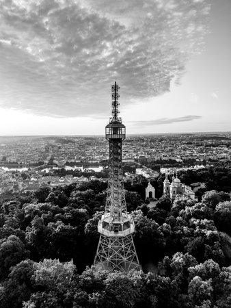 At sunrise, the Petrin Lookout Tower stands tall above the city of Prague, surrounded by lush greenery. The bright sky casts stunning colors over the landscape, creating a breathtaking view.の写真素材