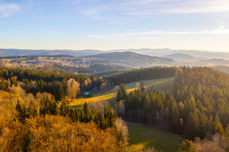 A sunny autumn morning unfolds over the Jizera Mountains, highlighting the Bramberk lookout tower and the surrounding vibrant forests. Natures beauty captivates the landscape in golden hues.の写真素材