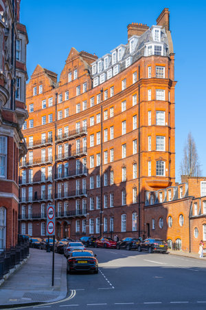Bright sunshine illuminates the striking red brick building in Kensington, London. The architectural style showcases intricate details typical of the areas historic charm.の写真素材
