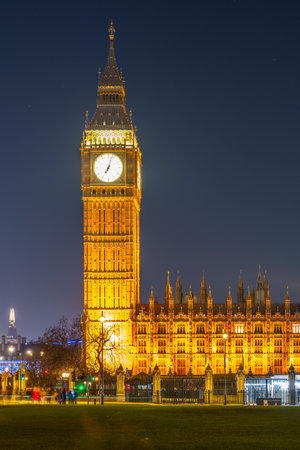 Big Ben stands proudly against the night sky, its clock face glowing brilliantly. The historic structure, surrounded by trees, showcases the beauty of London after sunset.の写真素材