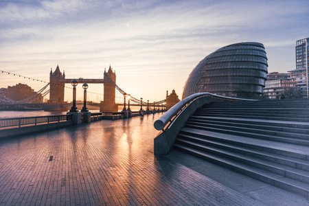 A beautiful morning at Queens Walk showcases Tower Bridge towering over the River Thames. Soft light casts reflections on the pavement, creating a serene atmosphere for walkers.の写真素材