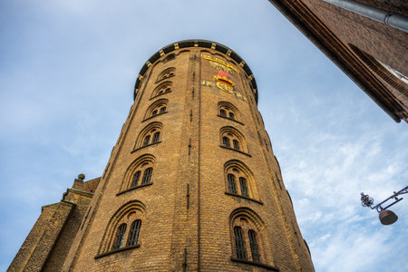 Tourists explore the Round Tower in Copenhagen, a historic building featuring a unique spiral ramp and stunning views from the top, enhanced by a bright blue sky and charming architecture.の写真素材