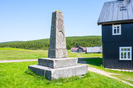 A stone pyramid stands tall in Jizerka Village, surrounded by lush green fields and mountains. Clear blue skies add to the serene atmosphere, revealing the charm of Czechias countryside.の写真素材