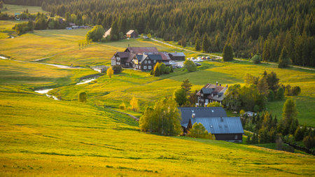 Evening light casts a warm glow over Jizerka Village in the Jizera Mountains. The tranquil landscape features fields, forests, and quaint houses surrounded by natures beauty.の写真素材