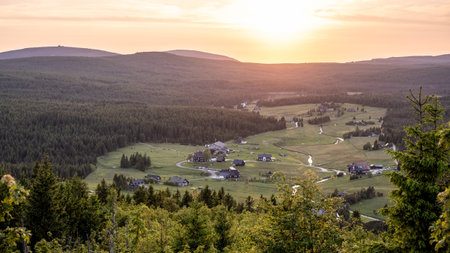 As the sun sets over Jizerka Village in the Jizera Mountains, the landscape glows with warm hues. The peaceful village rests amidst rolling hills and dense forests, evoking a sense of calm.の写真素材