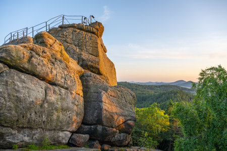 Golden sunlight bathes the sandstone cliffs of Popov Cliffs in Czechia during a tranquil evening. Lush greenery surrounds the striking rock formations in this serene landscape.の写真素材
