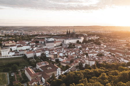 Golden sunlight bathes Prague Castle and the surrounding city at dawn. The vibrant rooftops glow as the first light breaks, showcasing a breathtaking panorama of historical architecture.の写真素材