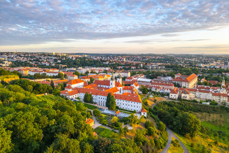 Strahov Monastery stands majestically at sunrise, illuminated by soft morning light. The vibrant rooftops contrast beautifully with the lush greenery, showcasing Pragues stunning landscape.の写真素材