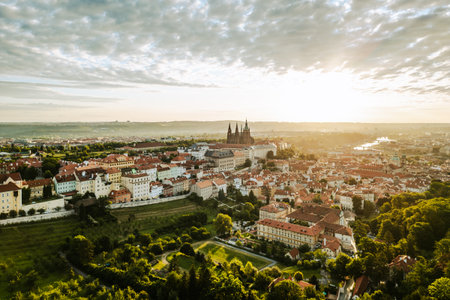 Golden sunlight bathes Prague Castle and the surrounding city as day breaks. The colorful rooftops and lush greenery create a captivating start to the day in this historic location.の写真素材