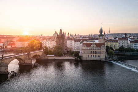 Sunrise casts a warm glow over Charles Bridge and the Vltava River in Prague, highlighting the citys...