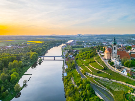 Aerial view captures Melnik city and its historic chateau perched above the tranquil Labe River. The golden hour illuminates the landscape, showcasing lush greenery and flowing waters.の写真素材