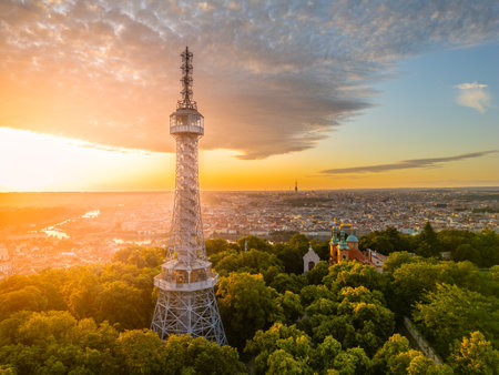 The Petrin Lookout Tower emerges against a vibrant sunrise in Prague, illuminating the skyline. This iconic structure is surrounded by lush greenery, offering a stunning view of the city.の写真素材