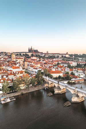 A breathtaking early morning view of Prague as the sun rises, illuminating the historic Charles Bridge and Hradcany Castle, with reflections dancing on the calm Vltava River.の写真素材